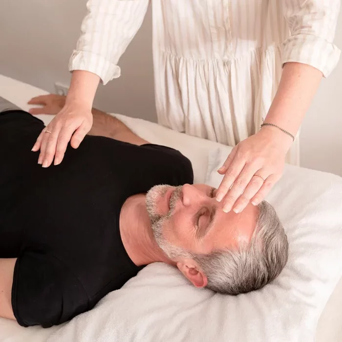 Ein Mann liegt entspannt auf einer Liege, während Heilpraktikerin Jessica Liebe mit sanften Berührungen am Kopf arbeitet – Symbol für mentale Befreiung, Stressabbau und Regeneration.