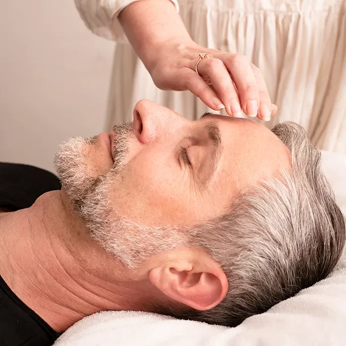 Ein Mann liegt entspannt, während eine Therapeutin sanft die Stirn berührt – Symbol für mentale Entlastung, Ruhe und Stressabbau im Führungskräfte-Coaching.