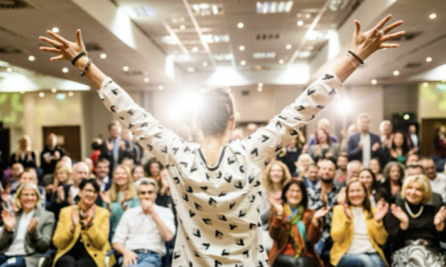 Jessica Liebe steht mit erhobenen Armen vor einem begeisterten Publikum während eines Gesundheitstags. Das Bild zeigt Motivation, Begeisterung und mentale Stärke im Rahmen der betrieblichen Gesundheitsförderung.